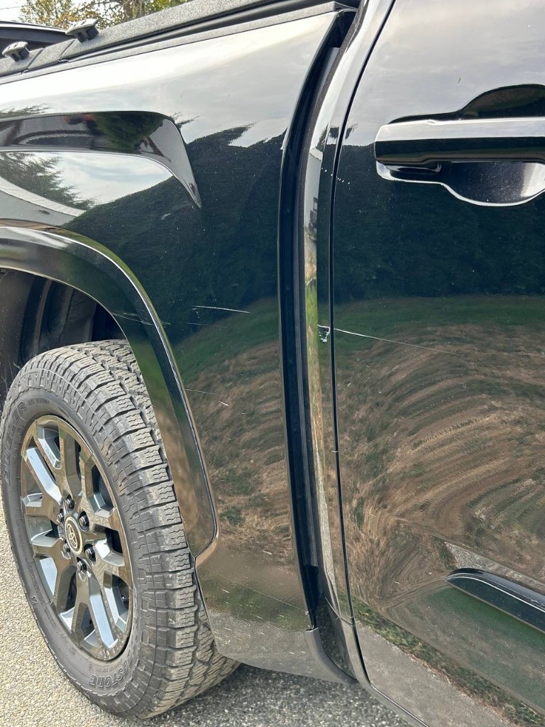 Black truck door before scratch removal, with visible horizontal scratches